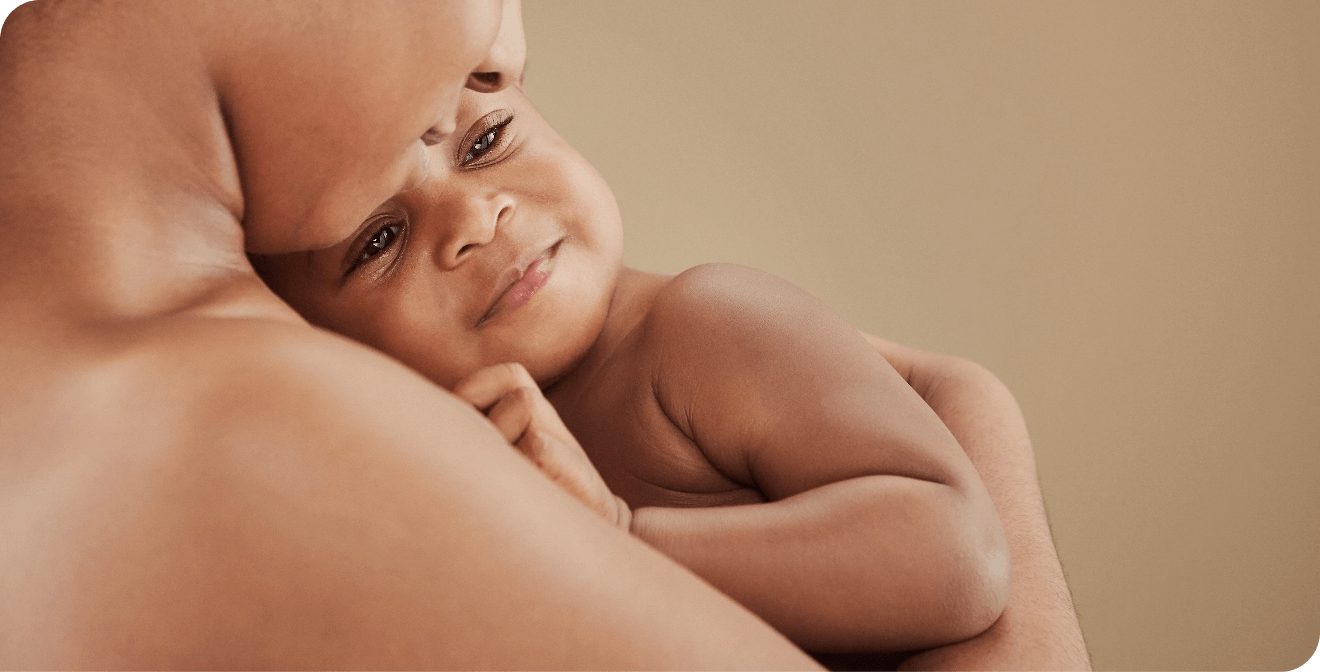 Een baby wordt liefdevol vastgehouden door een volwassene, tegen een warme achtergrond.