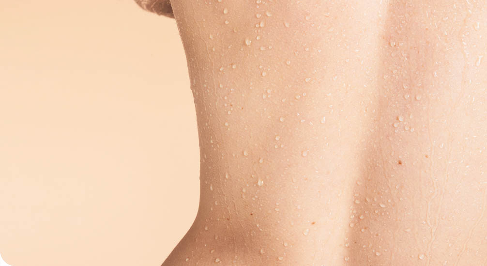 Close-up van de onderrug van een persoon met een lichte huidskleur. De huid is bedekt met kleine waterdruppeltjes.