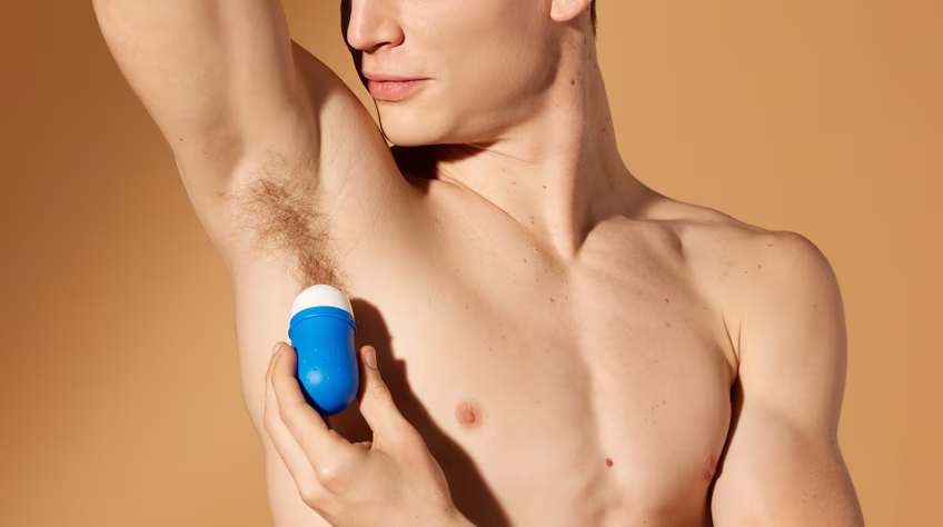 Een man met een ontbloot bovenlichaam die een blauwe roll-on deodorant aanbrengt onder zijn oksel.