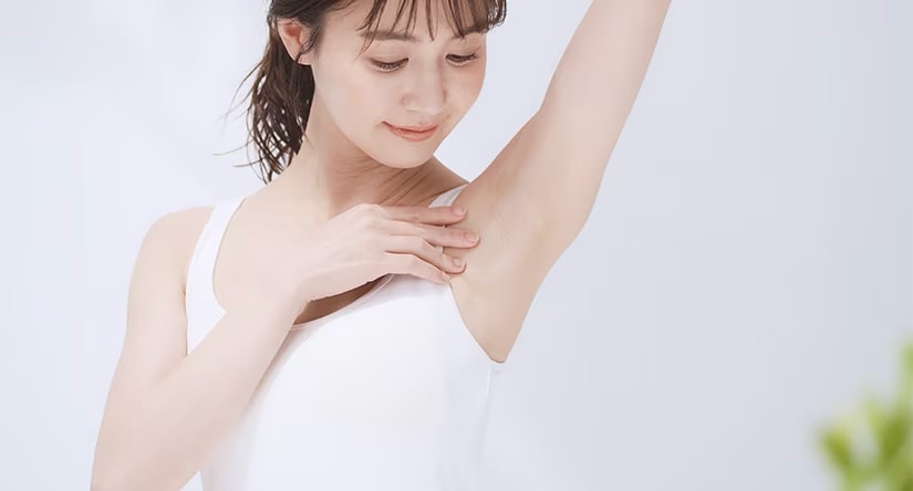 Een jonge Oost-Aziatische vrouw in een wit hemdje die haar oksel bekijkt en zachtjes aanraakt.