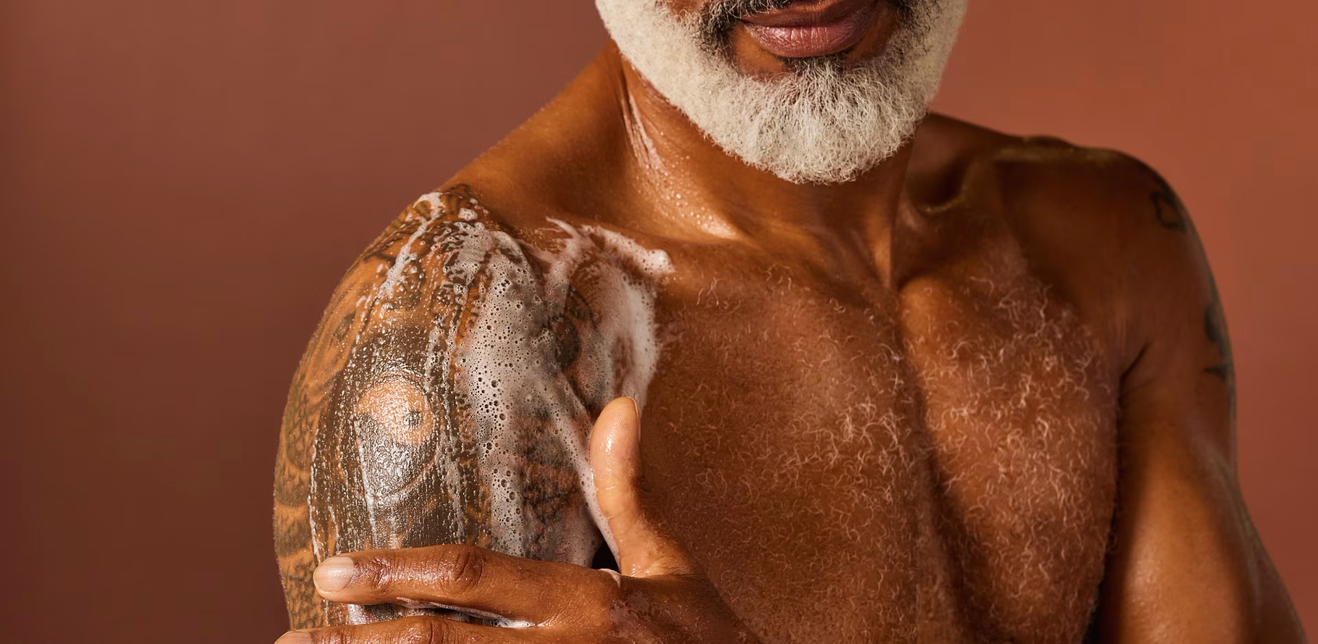Close-up van een oudere, gespierde zwarte man met een witte baard die zijn getatoeëerde schouder wast met zeepsop.