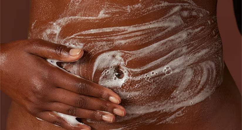 Close-up van de buik van een persoon met een donkere huid, die wordt ingezeept met een wit schuim.